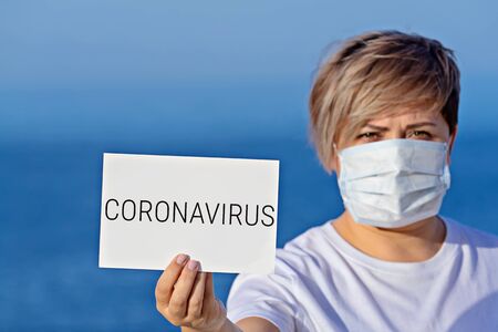 Blonde hair woman in protective surgical mask holds blank with text coronavirus 2019-nCoV. Concept of spread of Chinese Coronavirus 2019-nCoV virus around worldの写真素材