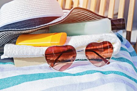 Closeuo of sunscreen cream cosmetic bottles, sunglasses and summer hat on deck chair. Accessories for sunbathing skin during sunbathingの写真素材