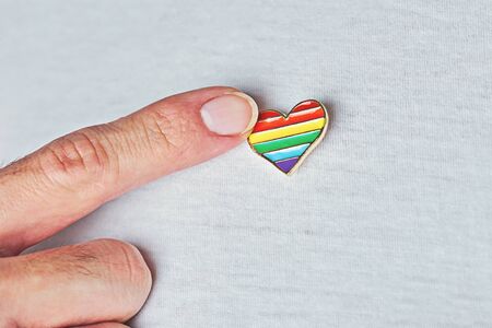 LGBT Pin badge in heart-shaped on white t-shirt and male forefinger. Concept of celebration of LGBTQ...