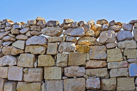 Limestone wall of brickwork with cracked boulders against blue sky background. Natural build texture with copy spacの写真素材