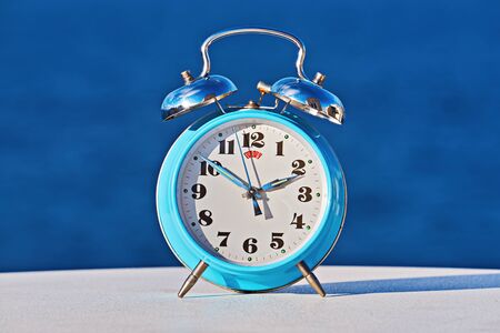 Blue alarm clock against sea background as spring forward and daylight saving concept. Abstract photo of changing time in spring. Turn time forward.の写真素材