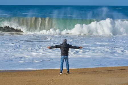 Rear view of man enjoying big wave of ocean on an empty sandy beach. Positive thinking and connecting with nature conceptの写真素材