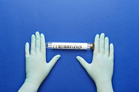 Hands in protective glove holds laboratory tube with abstract coronavirus on blue background.