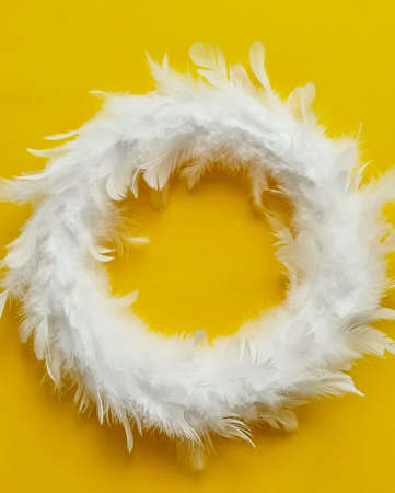 White feather wreath on yellow background with copy sapce, top view. Easter decorationの写真素材