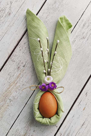 Decorative Bunny Ears from green napkin with egg on natural wooden background to Celebrate Easter,...
