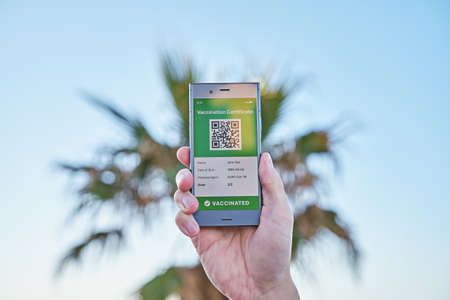 Smartphone in hand displaying on app mobile valid digital green vaccination certificate for...