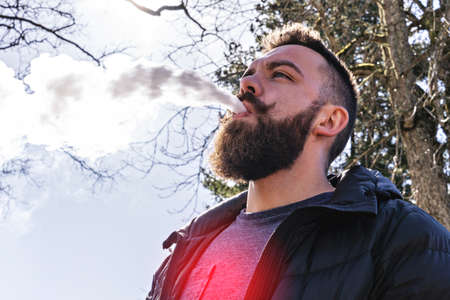 Bearded man vapes outdoors with red zone of pain on lungs as concept of danger of electronic...