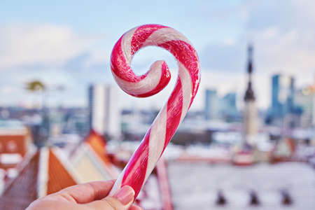 Striped candy cane lollipop in hand against old city of Tallinnの写真素材
