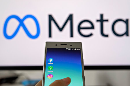 Smartphone display with logo of Facebook, WhatsApp and Instagram apps in hand against blurred META...