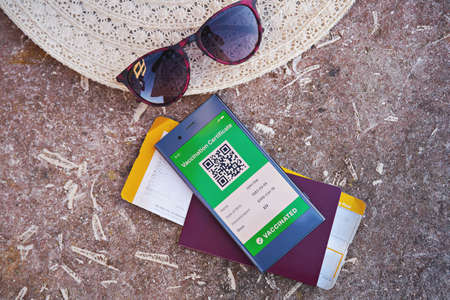 Smartphone displaying valid digital vaccination certificate for COVID-19, suitcase, summer hat, passport and boarding pass. Vaccination and health passport, international travel health controlの写真素材