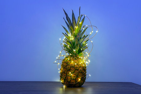 Pineapple with Christmas led-light garland on table, copy space. Zero-waste Christmas decor