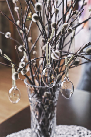 Crystal vase on table with bunch of willow sprigs decorated for Easter with decorative glass Easter...