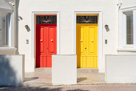 Red and yellow door side by side on white building facade, basking in sunlightの写真素材