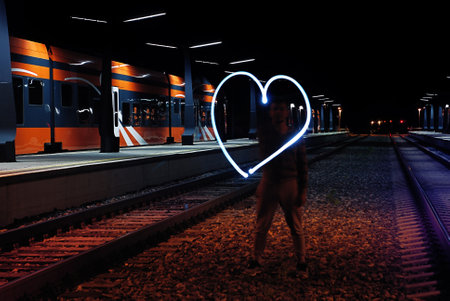 Artistic light painting of glowing heart on train tracks at modern station during nightの写真素材