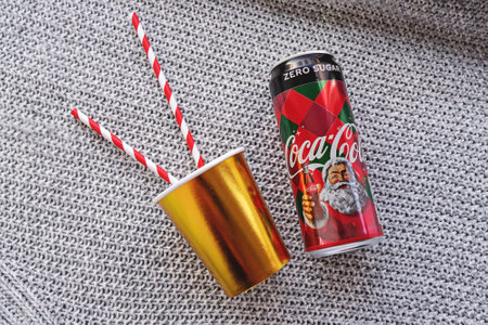 Drink Coca Cola can with golden paper cup with red and white striped straws on gray textured surface and snow: Tallinn, Estonia -30.11.2019のeditorial素材