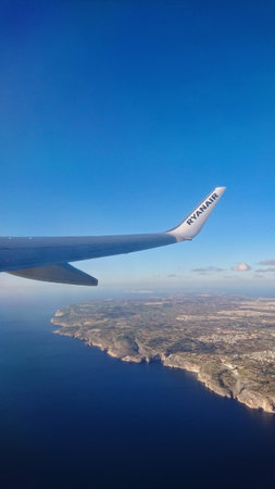 Ryanair airplane wing soaring over picturesque Maltese coastline cliff, showcasing deep blue sea and...