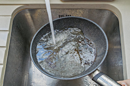 Hot nonstick pan under tap with water stream and foam, burnt bits washing away, active rinsing step...