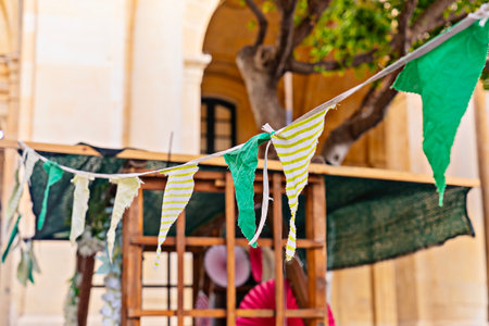 Close view of fabric bunting and pennant flags strung above market stall in urban courtyard,...