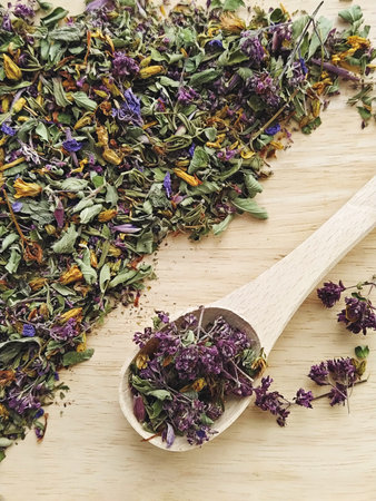 Dried herbal tea blend with mint, oregano and cornflower, colorful leaves and petals on wooden board with spoon, fragrant natural lookの写真素材