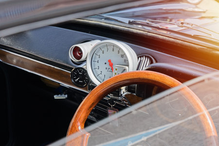 Close view of vintage car dashboard with wooden steering wheel, large analog tachometer and chrome...
