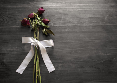 Withered roses with white bow on wooden backgroundの写真素材