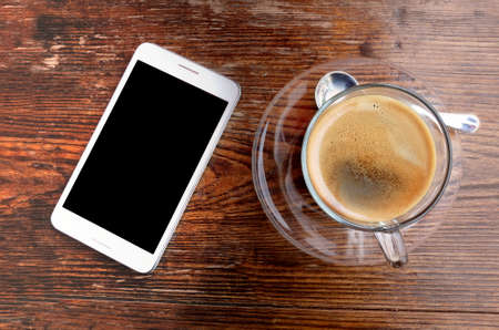 Coffee cup and smartphone on wooden office desk table.