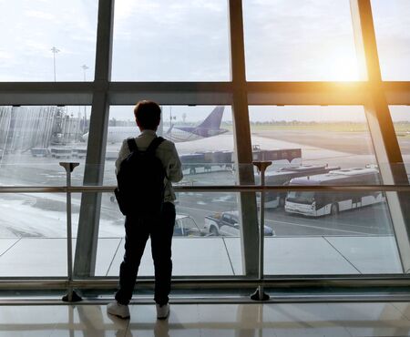 Travel concept. Young traveler with backpack at the airport looking through the window at  planes waiting for flight.の写真素材