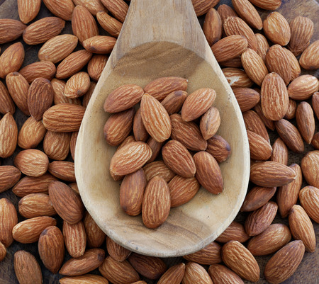 Almonds in wooden spoon on almonds background.の写真素材