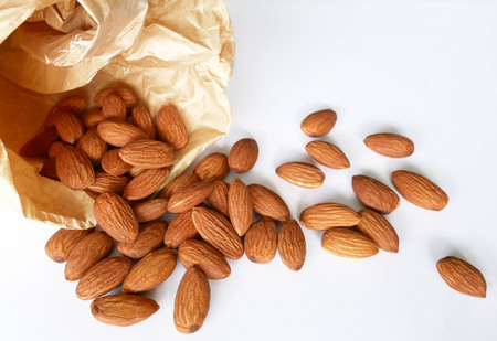 Almonds pour out of a paper bag on white background. Super nutritious and healthy food.の写真素材