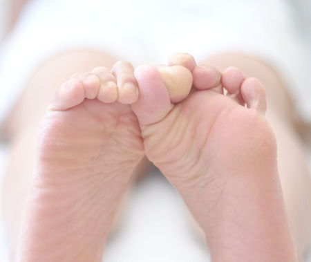Sleepy young woman rubbing her bare feet together in bed.の写真素材