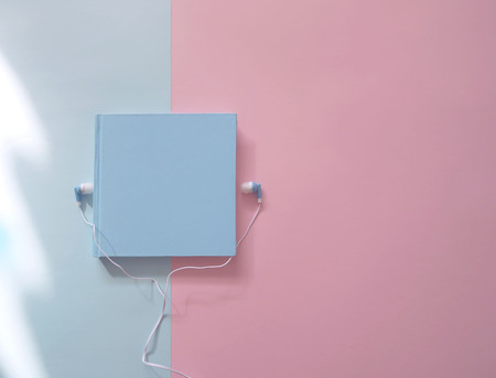 Book with earphones on a bue and pink background. Audio books conceptの写真素材