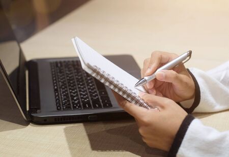 Business woman working on laptop and making note in a notebook. Online marketing, education, e-learning.の写真素材