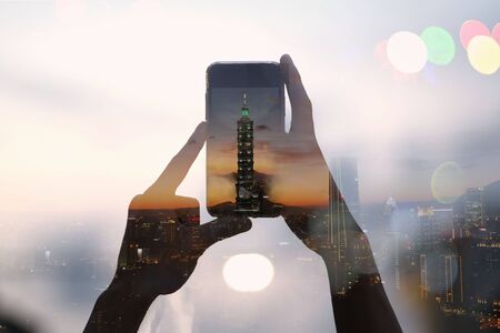 Double exposure of traveler taking picture with a smartphone and cityscape of Taipei 101 building, Taiwan.の写真素材