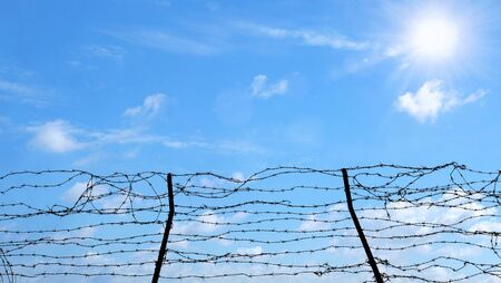 Barbed wire steel wall against the blue sky and sunshine light as a hope. Freedom, prison and hope concept.の写真素材
