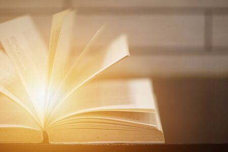 Light coming from open book on the desk over wooden background. Education learning concept.の写真素材