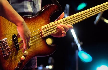 Professional musician plays electrical bass guitar solo on concert stage. Sring musical instrument...