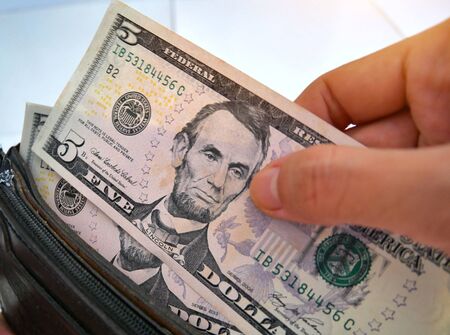 Hands taking 5 US dollars from open wallet.