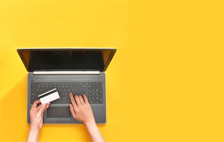Woman shopping online using laptop with credit card on yellow background.の写真素材