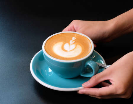 Waitress serving a cup of coffee with latte art to customer.の写真素材