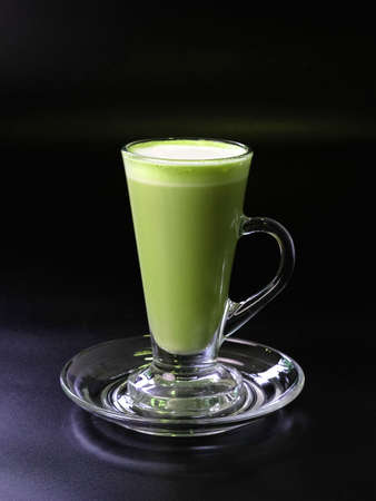 Matcha green tea latte in a tall glass on a dark background.の写真素材