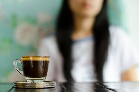 The cup of coffee (espresso) on the wooden table in the coffee shop with woman background
