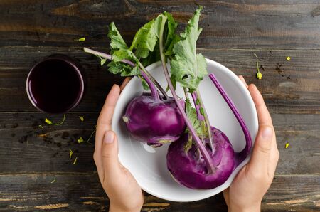 Purple kohlrabi in the bowl hold by hand on wooden backgroundの写真素材
