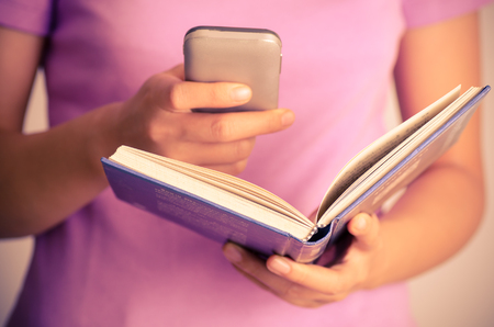 Close up of woman using smart phone for search on bookの写真素材