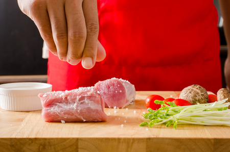 Chef's hand pour salt on raw pork and mix with vegetables for cooking roast porkの写真素材