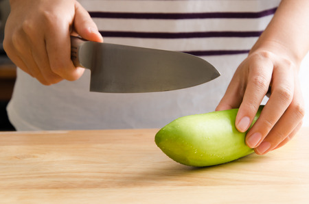 Woman chopping green eggplant on wooden board prepare for cookingの写真素材