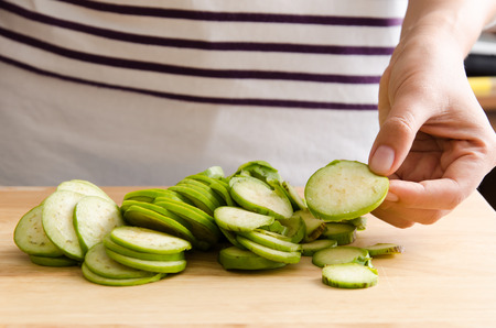 Woman holding sliced green eggplant on wooden board prepare for cookingの写真素材