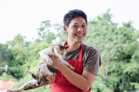 Portrait of Asian man wear red apron playing with catの写真素材