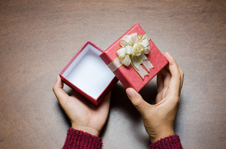 Woman hand opening red gift box on wooden background