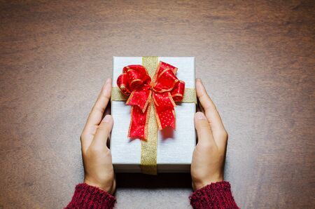 Woman holding gift box by hand on wooden background to giving in special day