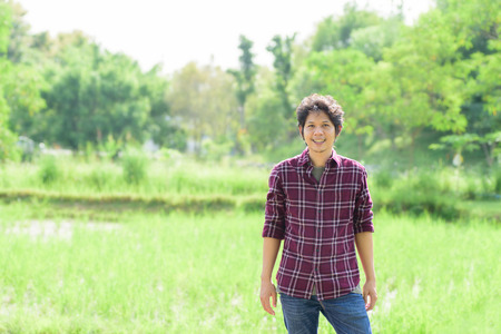 Asian young farmer standing in green fieldの写真素材
